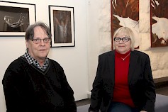 Esko Soinin ja Marita Erkkola-Järvisen takana vasemmalla Soinin taidevalokuvia ja oikealla Erkkola-Järvisen akryylitöitä.