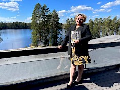 1. Ähtärin Zoon toimitusjohtaja Arja Väliaho seisahtui Mesikämmenen terassille, josta näkyy upea Ähtärin luonto ja järvi. Väliaho muistuttaa, että Panda –talon uusi nimi julkistetaan ympäristökasvatuskeskuksen avajaisten yhteydessä 7.6.