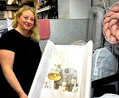 Jonna Koskimäki-Puska esittelee vauvan hoitoalustaa, missä viehättävä kuva kiinnittää huomion. Hän kertoo, että varastossa pyritään pitämään hinta-laatusuhteeltaan hyviä tuotteita ja toivottaa lapsiperheet lastentarvikeostoksille, joko verkon kautta tai suoraan varastomyymälään Ilmajoen Pojanluomalle.