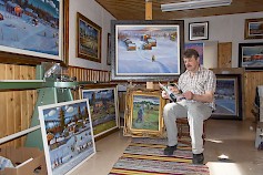 Taiteilija Reijo Kivijärvi maalaustensa keskellä sylissään omakustantama kirja ELÄMÄNI ON TAITEILUA